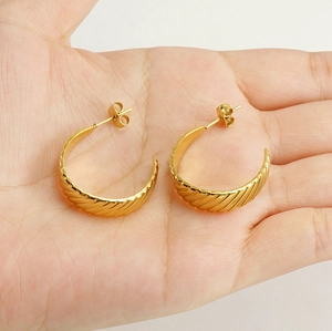 Detailed close-up of textured 18K gold-plated titanium steel C-shaped earrings held by hand