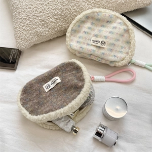 Detail of plush shell-shaped cosmetic bags in fleece textures on white bedding
