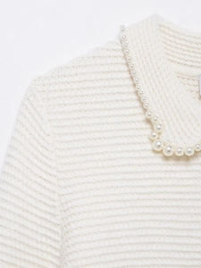 Gros plan d'un cardigan blanc en maille avec des perles le long de l'encolure
