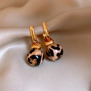 Detail of gold metal earrings with leopard print spherical pendants on silk fabric