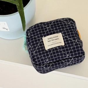 Detailed shot of a navy blue checkered quilted pouch with an orange zipper and tassel