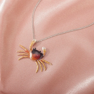 Primer plano del collar con colgante de cangrejo en esmalte naranja y negro vibrante
