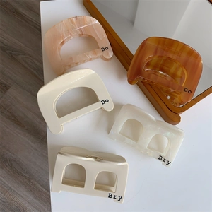 Flat lay of acetate shark hair clips in beige and amber with D and B letter prints