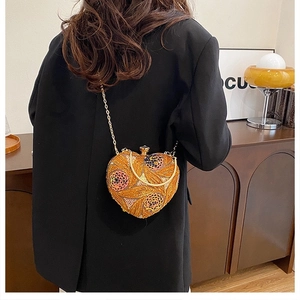 Macro detail of the heart-shaped orange sequin bag with elegant gold chain and handle