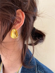 Close-up of golden irregular textured stud earring worn on model for size and detail
