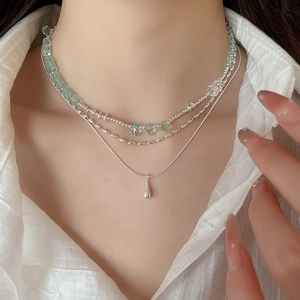 Detail of a three-layer layered necklace featuring green beads and a silver teardrop pendant