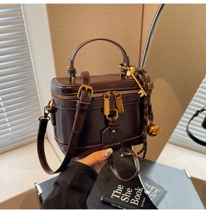 Close-up of deep brown leather bucket bag with gold zipper and bell charm accessories