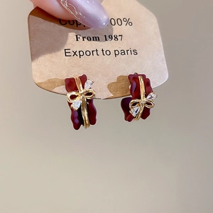 Detail of red flower petal earrings with gold bow and zircon on display card