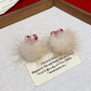 Detail of plush beige pompom earrings with red plaid heart charm on wooden tray