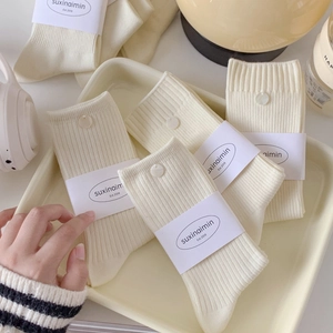 Creamy white knitted crew socks with decorative pearl buttons in a cozy lifestyle setting