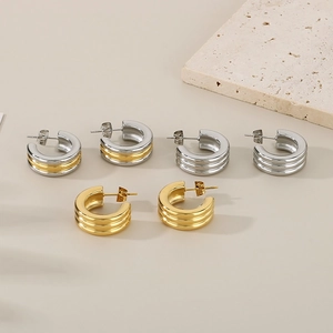 Detailed view of triple hoop earrings in gold and silver finishes on a stone background