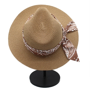 Close-up of khaki straw sun hat with patterned ribbon on a black metal display stand