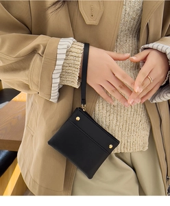 Close-up of a black leather mini coin purse with wrist strap and gold stud detailing