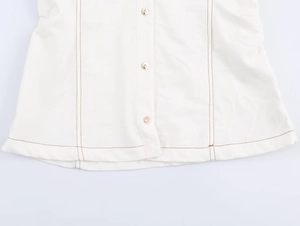 Detail van wit denim overhemd met gouden knopen en bruine contrasterende stiksels