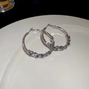 Elegant silver-colored geometric hoop earrings with shimmering crystal pavé on a white plate