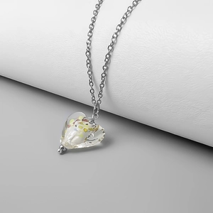 Macro detail of a clear heart pendant with colorful foil flakes on a silver chain