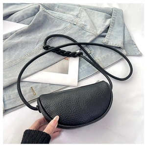 Detail of black pebbled leather saddle bag with woven knot strap on denim fabric