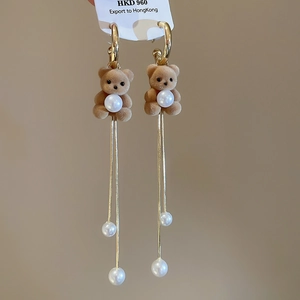 Detail of flocking bear earring with pearls and long gold snake chains on brown background