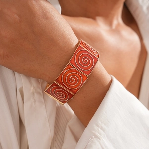 Close-up of orange enamel wide bracelet with vintage golden spiral patterns on wrist