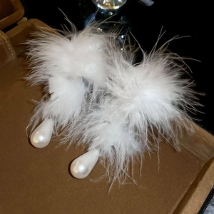 Macro shot of elegant white feather earrings featuring glossy teardrop pearls on dark leather