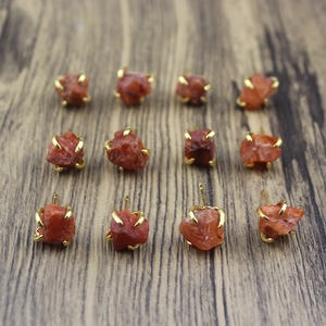 Macro view of natural red raw stone earrings with gold claw settings on wood base