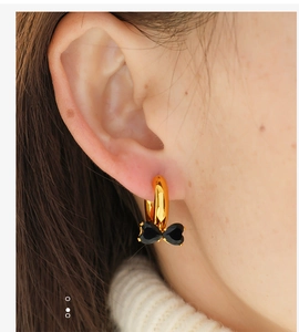 Close-up of a gold huggie hoop earring with a black crystal bow pendant on a model