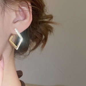 Close-up detail of a minimalist gold geometric diamond-shaped drop earring on a model