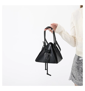 Detail of black punk style crossbody bag with metal chain and cross charm on model