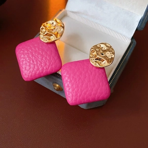 Detail of irregular golden hammered metal stud and square magenta leather drop earring