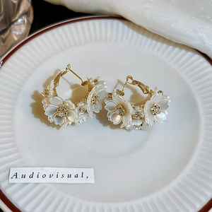 Close-up of golden flower earrings with white petals and crystals on a ceramic plate
