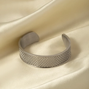 Macro detail of silver fish scale textured open bangle on champagne silk fabric