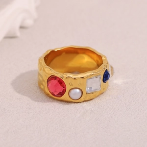 Macro view of gold plated wide band ring with colorful stones, pearls and hammered texture
