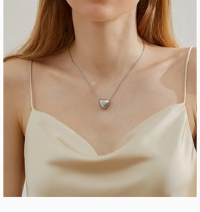 Detailed close-up of a minimalist silver heart pendant necklace worn on a silk dress