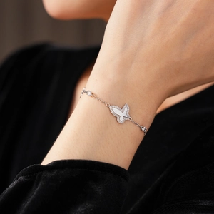 Close-up of a silver butterfly charm bracelet with white inlay on a female wrist