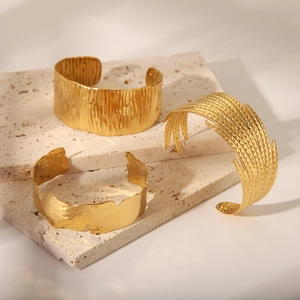Détails de trois bracelets joncs dorés en acier inoxydable texturé sur plaques