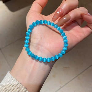 Close-up of sky blue cat eye stone beaded bracelet held by hand in soft light