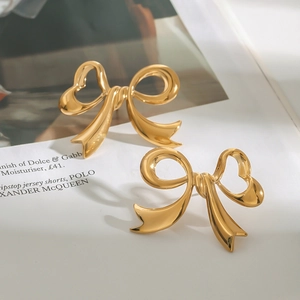Elegant gold bow-shaped stainless steel stud earrings on a fashion magazine background