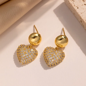 Macro shot of gold heart earrings with white cubic zirconia pavé stones on beige background