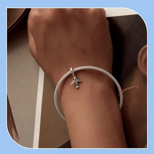 Detail of silver mesh bracelet with miniature airplane charm on a lifestyle background