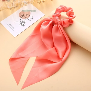 Close-up of coral pink satin scrunchie with long ribbon tails and silky texture