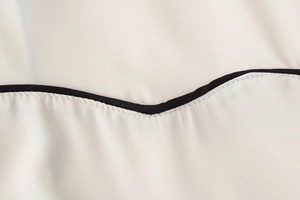 Détail d'une robe chemise sans manches avec liseré noir contrasté et coutures blanches précises
