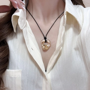 Detailed close-up of hollow gold irregular circular pendant on a black cord necklace