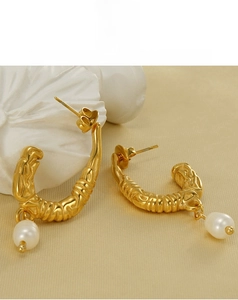 Detail of U-shaped gold earrings with textured metal finish and round white pearl drop