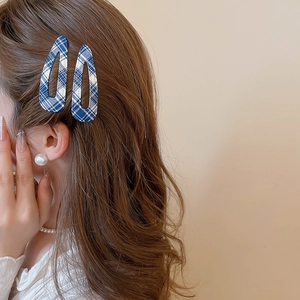Dettaglio di donna con fermagli per capelli a quadretti blu e orecchino di perla grande
