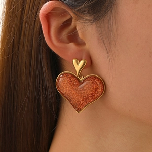 Gold-plated stainless steel heart earrings with orange glitter resin pendant on model