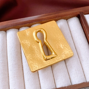Detailed macro shot of vintage gold square brooch with a central keyhole and hammered texture