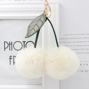 Close-up of white cherry-shaped faux fur keychain with green leaves and gold clasp