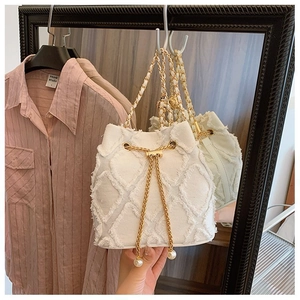 Detail of white diamond quilted bucket bag with gold chain and pearl charm accessory