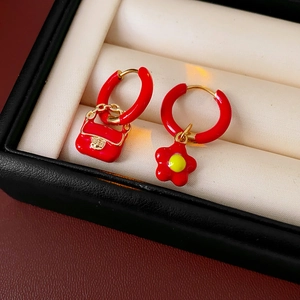 Detail of gold titanium earrings with red enamel flower and mini handbag charm in a box