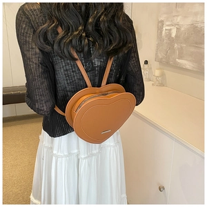 Brown heart-shaped backpack on model featuring sleek PU leather and metallic details